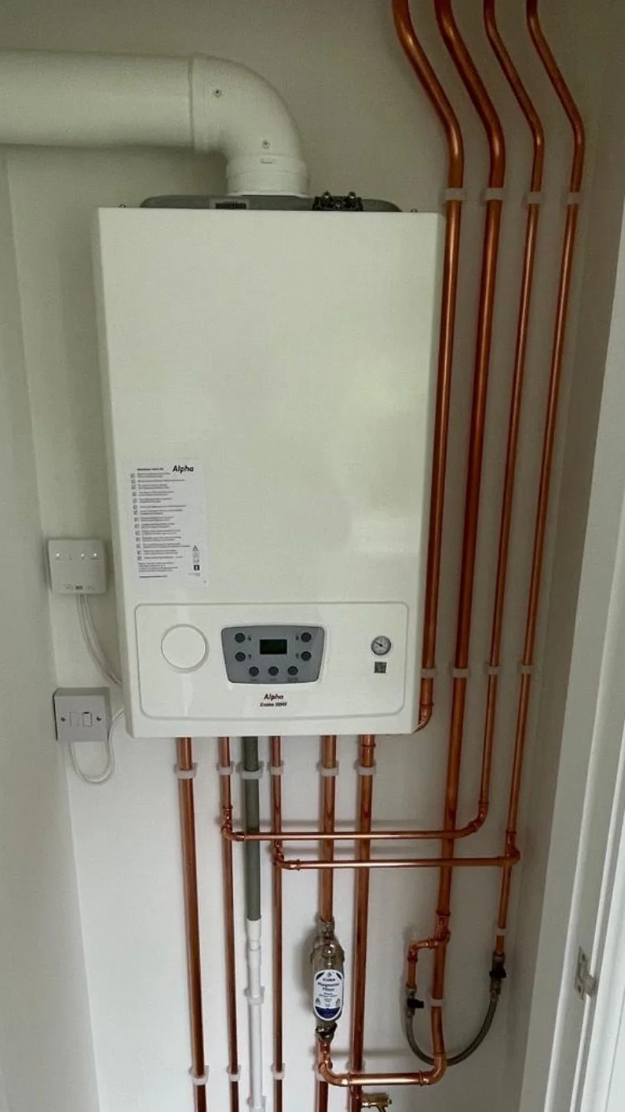 Alpha Evoke combi boiler installed with four polished copper risers and a magnetic system filter