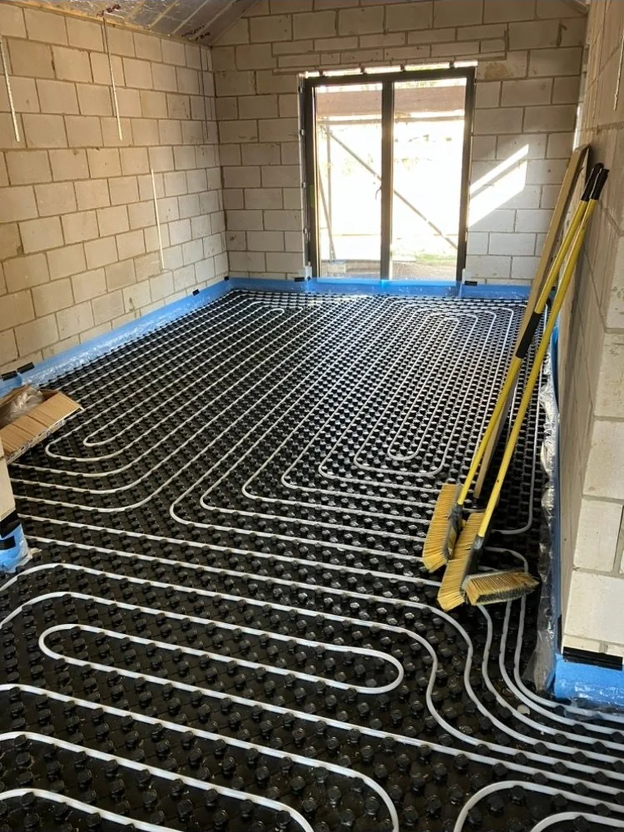 Wet underfloor heating pipe laid in loops across a full room on black castellated insulation panel