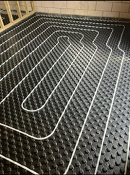 Wet underfloor heating pipe clipped into castellated insulation panel across a room